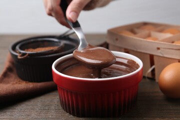 Woman with liquid chocolate dough in bowl at wooden table, closeup