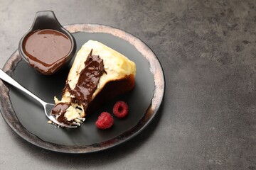 Piece of delicious Basque cheesecake with chocolate sauce and raspberries on grey table, closeup. Space for text