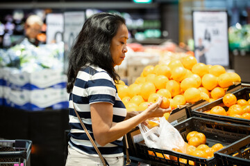 A middle-aged asian woman shopping for fresh mandarins in a supermarket, symbolizing healthy eating, real life, diversity, and everyday business.