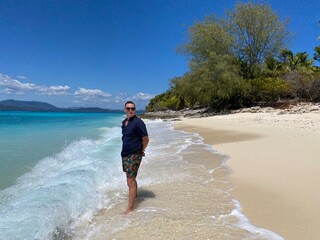 A man standing on a tropical island in Madagascar across clear turquoise waters. The bright sunlight reflects on the calm ocean, highlighting the white sandy shores and creating a pe