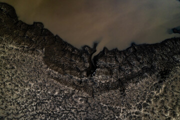 Water puddle edge cracked mud aerial detail view mining area industrial texture pattern brown beige environmental landscape abstract surface sediment