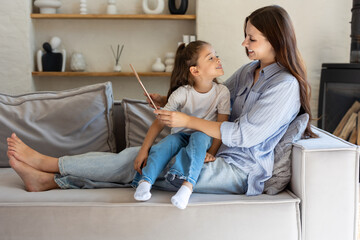 Mother and girl enjoying online activity with tablet in living room