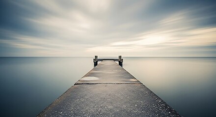 A long wooden pier extends into the calm lake at sunset, meeting the horizon beneath a colorful sky