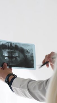 Dentist in a white coat discussing a panoramic dental x-ray with a female patient, using a pen to indicate the jaw and teeth in a state-of-the-art dental office