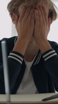 Desperate young teenage boy crying and holding his head in his hands while sitting at a desk in a hospital room, struggling with bad news, mental health issues, and despair