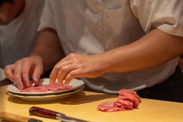 Chef preparing thinly sliced meat on plate in professional kitchen setting
