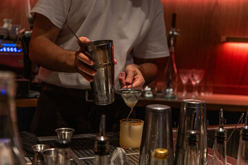 Bartender preparing cocktail with shaker and strainer in modern bar setting