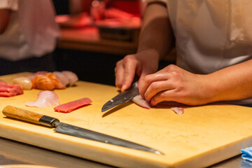 Skilled chef preparing sushi with fresh fish on wooden cutting board