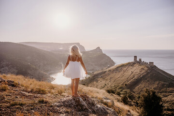 Fototapeta premium A woman stands on a hill overlooking a body of water. The sky is clear and the sun is shining brightly. The woman is enjoying the view and the peaceful atmosphere.