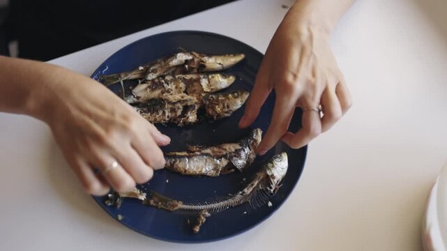 Woman cleaning grilled sardines on blue plate