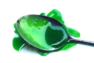 spoon containing thick green liquid with some drops and splashes around it on a clean white background