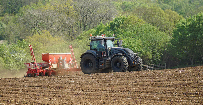 Tractor pulling seed drill on field trees in background