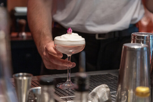Bartender serving cocktail with whipped cream and decorative garnish