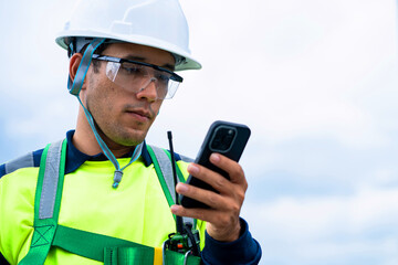 A man in a yellow and green safety vest is looking at his cell phone