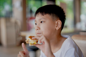 young boy is eating a sandwich, Asian boy is happily eating food