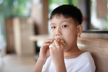 young boy is eating a sandwich, Asian boy is happily eating food