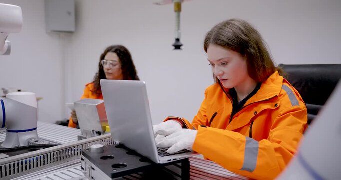 female adult technician asian using laptop during automation training session in robotics lab while managing control panel connected to robotic arm in smart industrial engineering environment