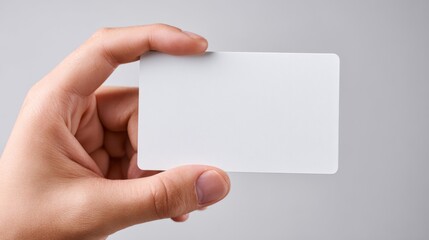 Obraz premium A close-up of a hand holding a blank, white card against a light gray background, symbolizing potential and opportunity.