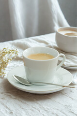 A delicate cup of tea on a saucer with a spoon and soft fabric background