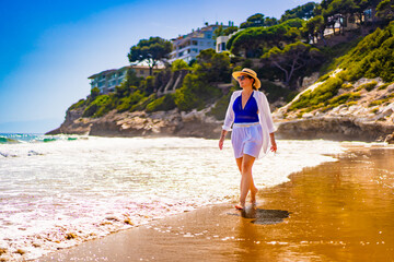 Beautiful middle aged woman walking on sandy beach on sunny summer day