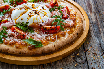 Pizza with cured ham, burrata cheese, tomatoes and arugula on wooden table