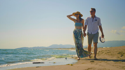 Happy couple enjoying a romantic walk along a sandy beach at sunset, holding hands while exploring the coastline during their relaxing summer holidays