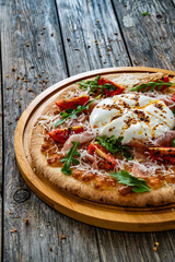 Pizza with cured ham, burrata cheese, tomatoes and arugula on wooden table