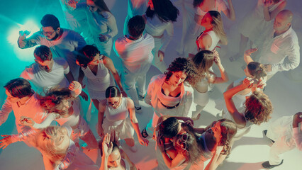 Top view of crowd dancing at white party under bright stage light. Concept of social lifestyle culture, collective energy of modern generation, commercial visuals for entertainment and events.