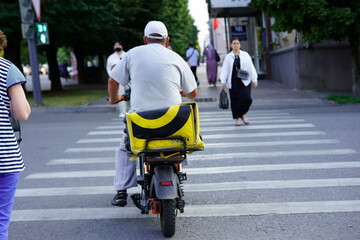 Bicycle delivery driver crossing a street with pedestrians and traffic signals in an urban area...