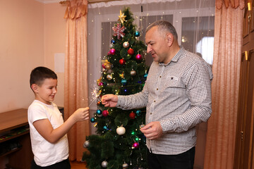 Father and son lighting sparklers near the Christmas tree, celebrating Christmas or New Year.