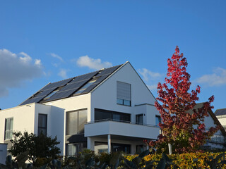 Many photovoltaik modules for green electrical energy production covering the roof of a beautiful new built house with blue sky