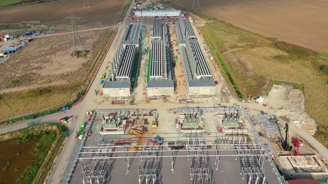 Top-down drone exploration of a renewable energy hub: wind turbines, solar panels and battery storage facility under construction near Tilbury, UK