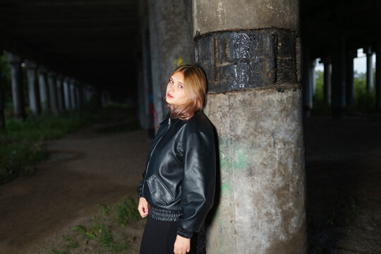 Person in leather jacket standing under bridge with urban background