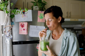 Woman drinking healthy smoothie from straw at home