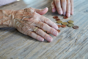 Hands of senior woman counting coins at wooden table