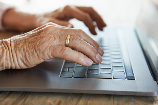 Hand of senior woman typing on keyboard of laptop, close-up