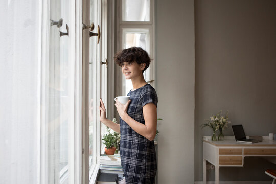 Portrait of smiling young woman looking through window at home