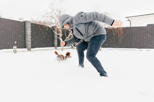 Man chasing dog outdoors playing in snow during winter