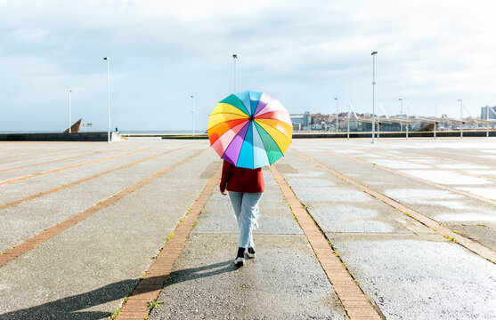 Woman walking with multi colored umbrella on footpath during sunny day