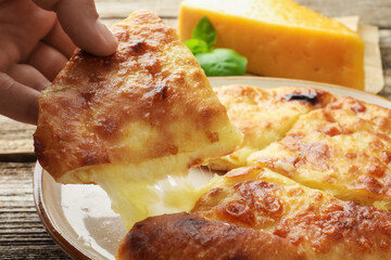 Woman taking piece of delicious Megrelian khachapuri at wooden table, closeup