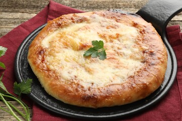 Delicious Megrelian khachapuri with parsley on wooden table, closeup