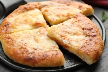 Cut delicious Megrelian khachapuri on black table, closeup