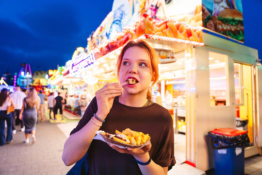 Girl enjoying french fries at amusement park with neon lights