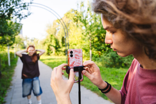 Teen recording friend with smartphone outdoors for social media content