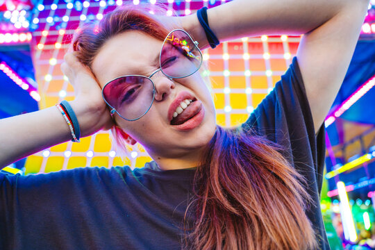Excited young girl posing with sunglasses at neon-lit amusement park at night