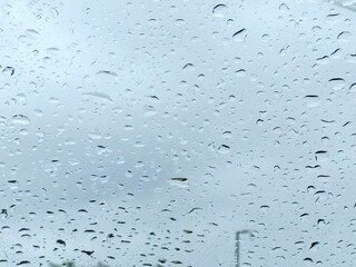Rainy day concept with water drops covering a window, looking out at an overcast sky