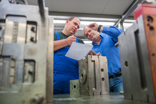 Two men discussing a metal workpiece