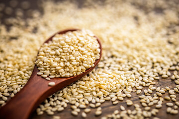 Roasted sesame seeds on spoon on wooden table.