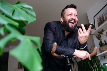 Happy businessman talking on speaker phone leaning on bicycle handle at home