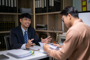 Two men are sitting at a desk, one of them is reading a document